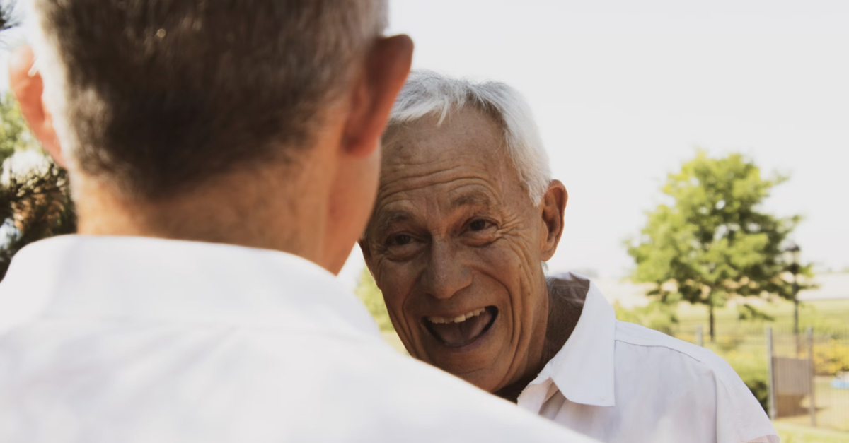 senior laughing at young person standing outside green tree in the back